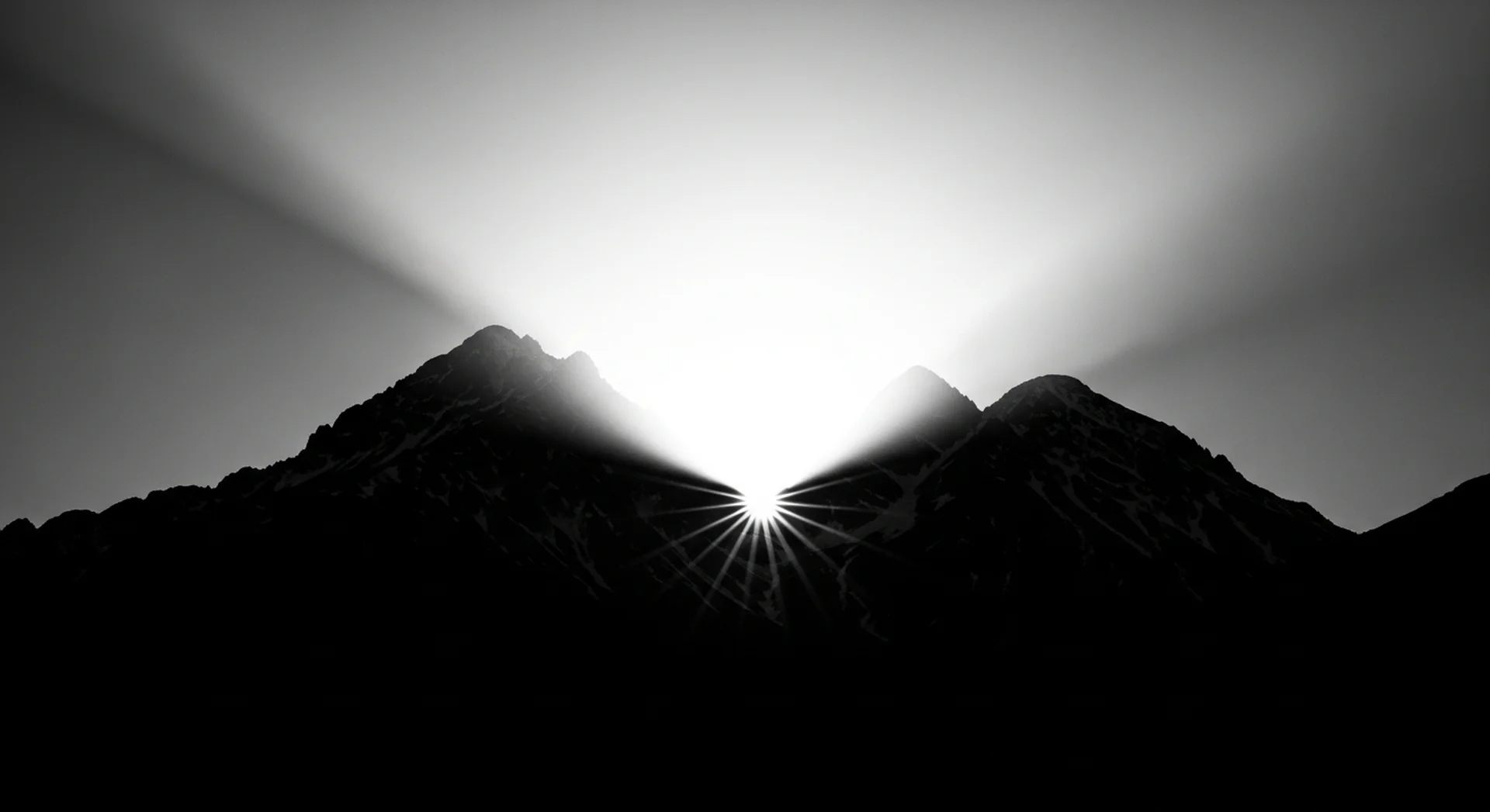 깊은 산맥 사이로 강렬한 빛이 터져 나오는 순간, 어둠에서 새로운 가능성으로의 전환을 상징하는 흑백 풍경